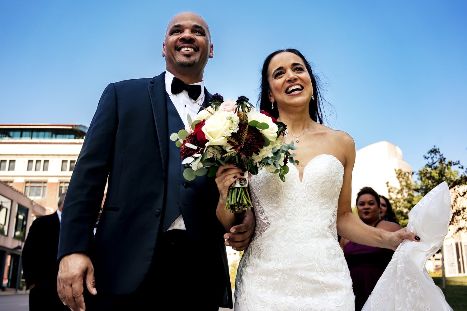 A colorful, candid picture of a bride and groom walking side by side, with big smiles on their faces on the day of their timeless summer wedding at The Station in Kansas City. 