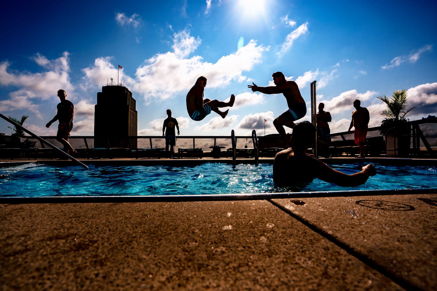 A colorful, candid picture of two men jumping into a rooftop pool on a summer wedding morning in downtown Kansas City. 
