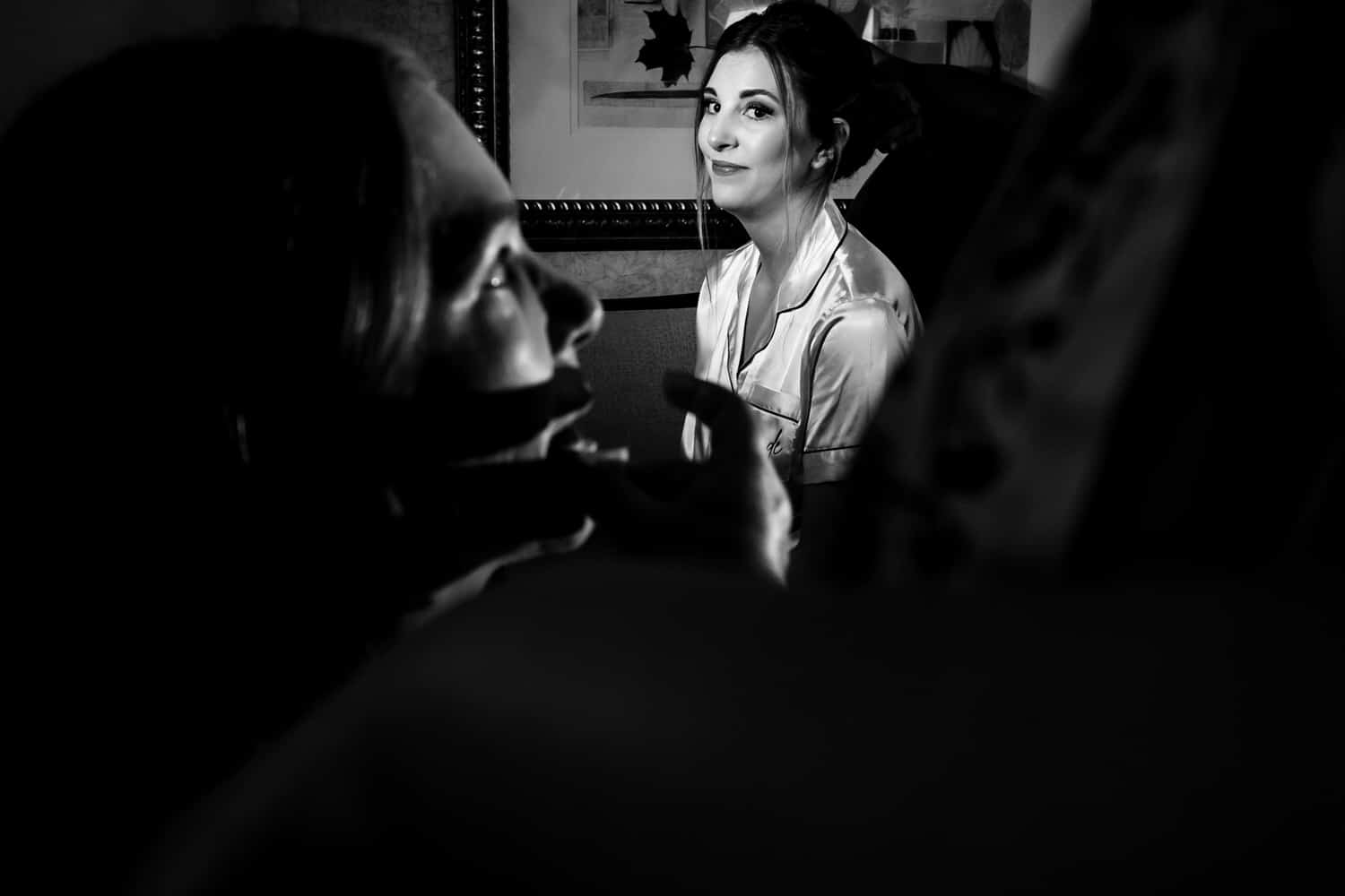 A candid black and white picture of a woman watching her mother get her makeup done on the morning of her Kansas City wedding. 