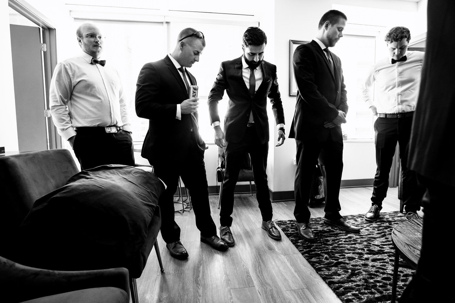 A candid black and white picture of a group of men all looking each other over to make sure they're dressed appropriately. 