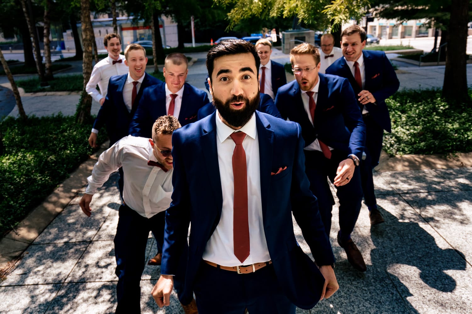 A colorful, candid picture of a groom with a surprised look on his face as a group of groomsmen run towards him on the morning of a summer wedding in Kansas City. 