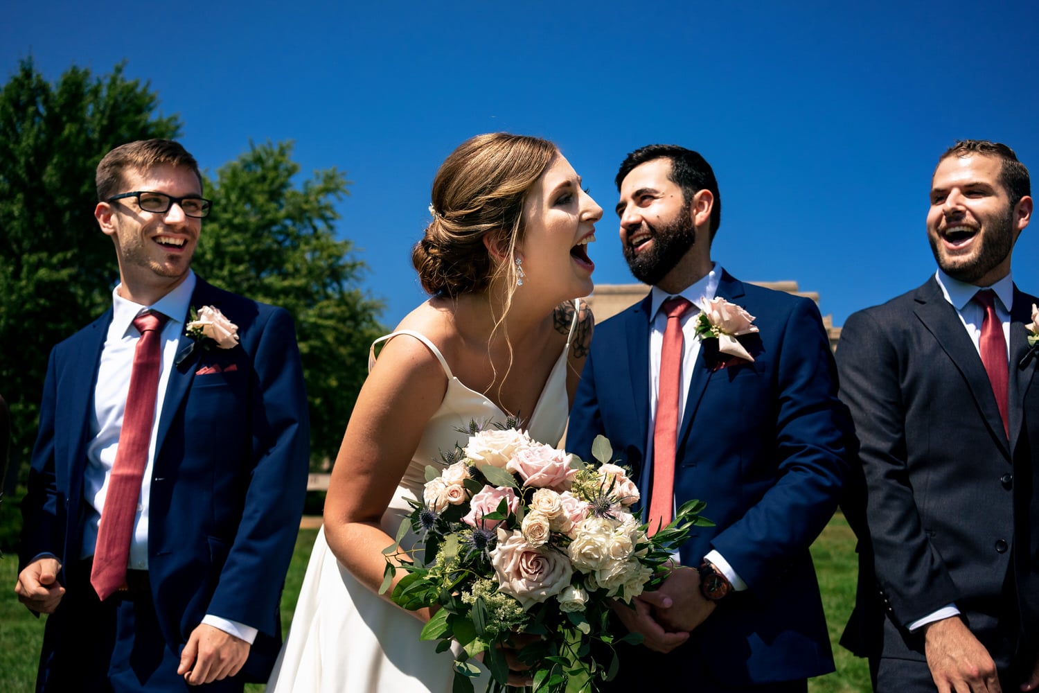 A colorful, candid picture of a bride, groom, and their wedding party laughing out loud on a summer wedding day  in Kansas City. 