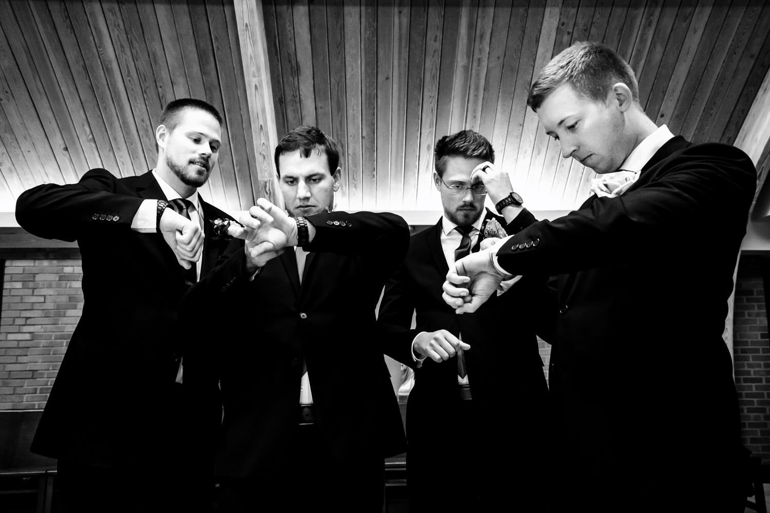 A candid black and white picture of a group of four groomsmen all checking their watches on a summer wedding day. 