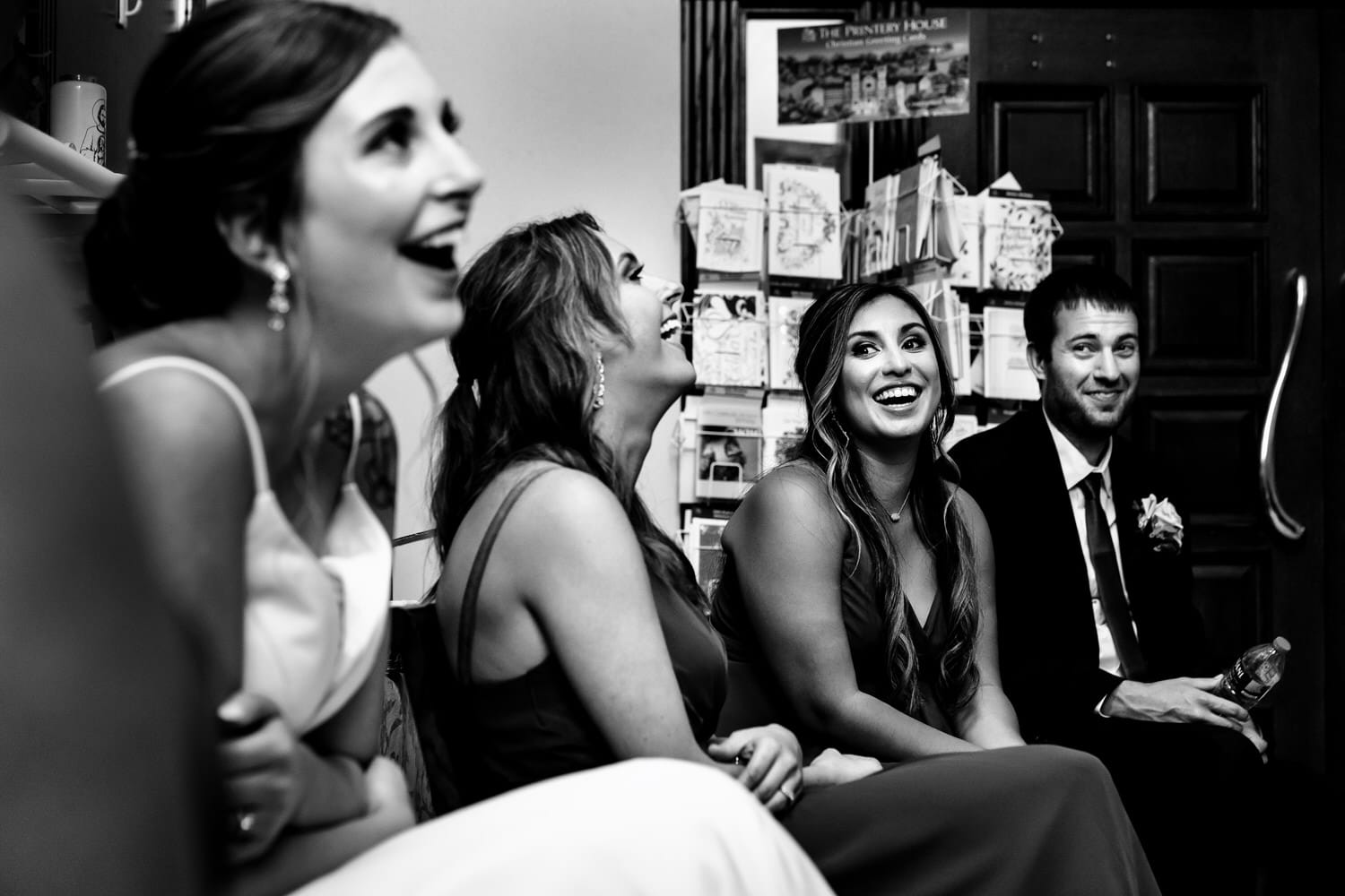 A candid black and white picture of a bride and her bridesmaids laughing together as they wait to walk down the aisle on a summer wedding day. 