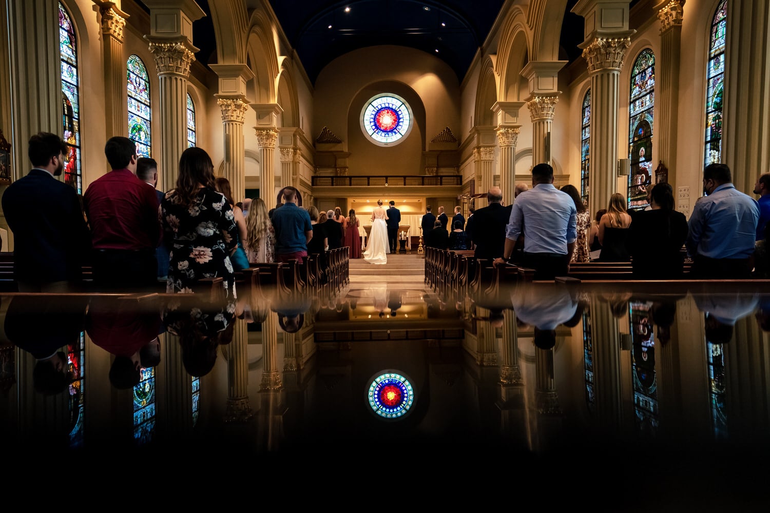 A colorful, wide photo of a bride and groom standing at the front of the Cathedral of the Immaculate Conception during a summer wedding ceremony in Kansas City. 