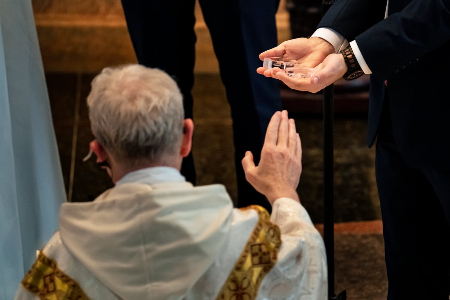 A close-up picture of a Catholic priest blessing wedding bands that a man holds in his hands during a summer wedding ceremony at The Cathedral of the Immaculate Conception in downtown Kansas City. 