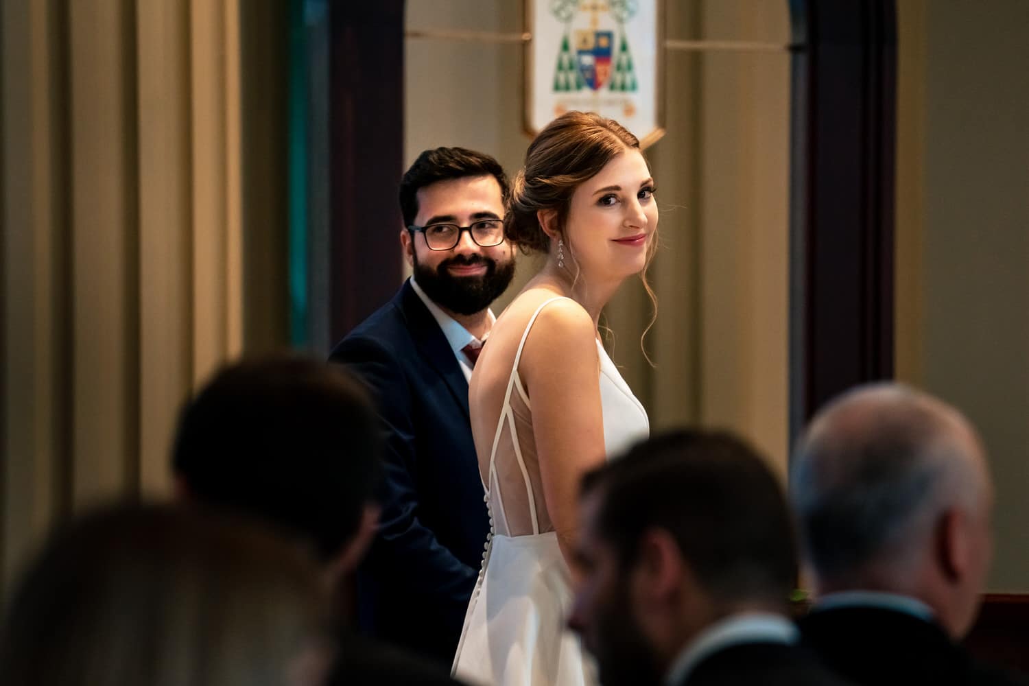 A colorful, candid picture of a bride and groom smiling, looking back at their wedding guests during a summer wedding ceremony at The Cathedral of the Immaculate Conception. 