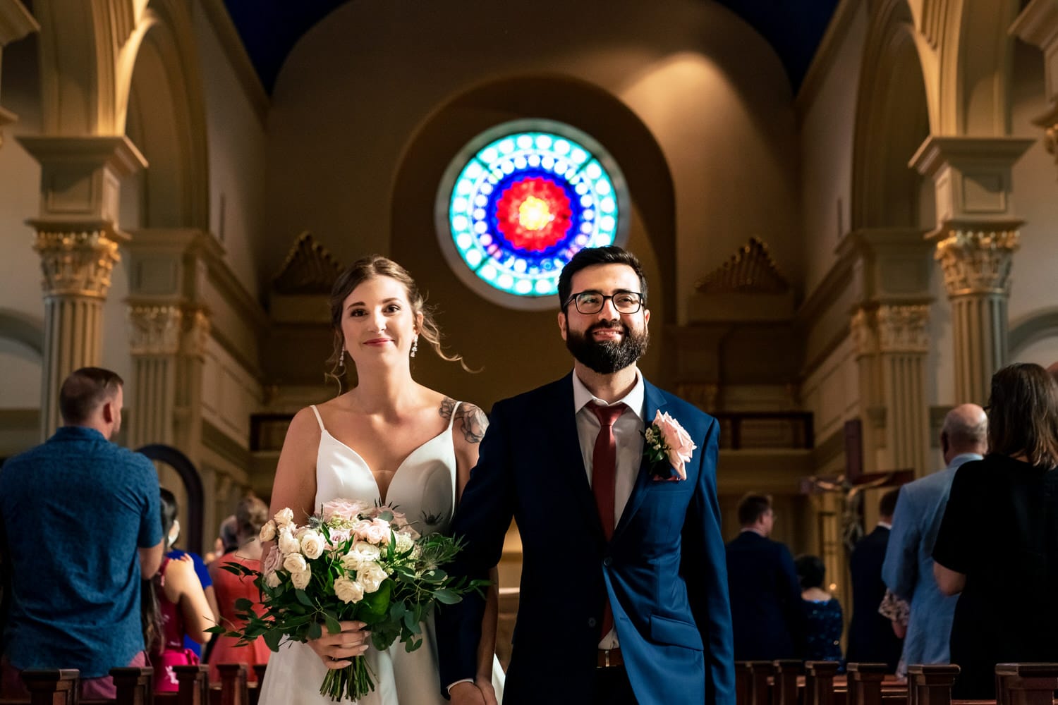 A colorful, candid picture of a bride and groom holding hands, walking back up the aisle after their wedding ceremony at The Cathedral of the Immaculate Conception in downtown Kansas City. 
