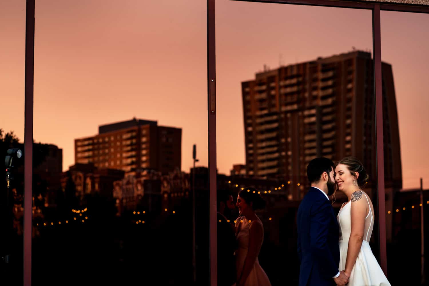 A close-up picture of a bride and groom sharing a kiss, the Kansas City Plaza skyline visible in the windows behind them on a summer wedding day in Kansas City. 