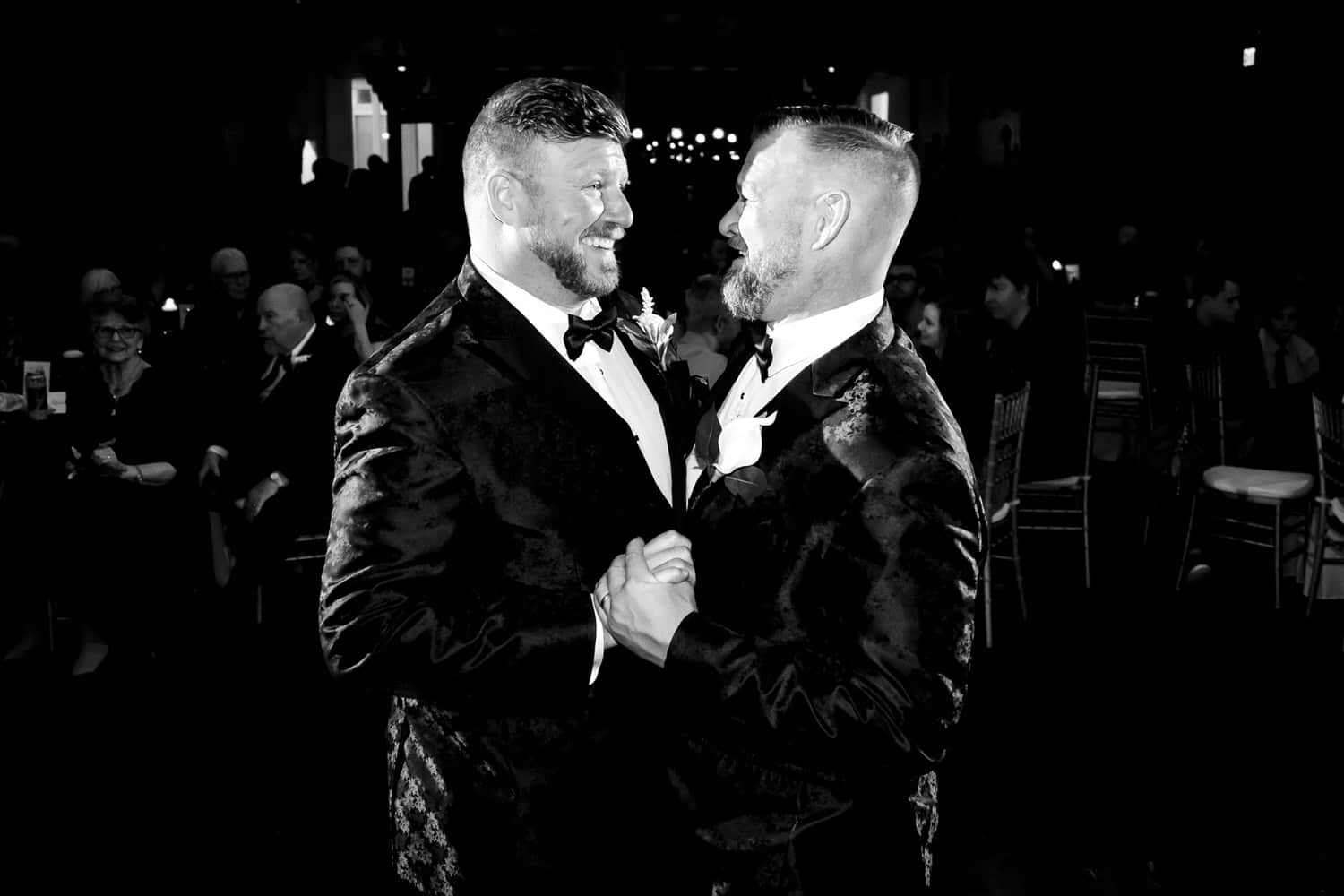 A candid black and white picture of two grooms dancing together during their fall wedding reception at The Madrid in Kansas City. 