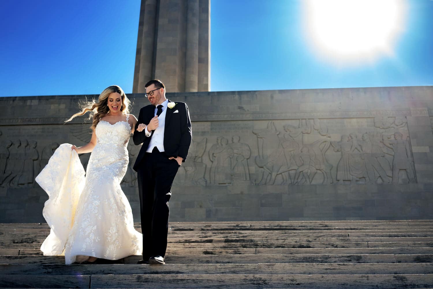 A colorful, candid picture of a bride and groom walking arm in arm down a set of stone stairs at Liberty Memorial on their October wedding day in Kansas City. 