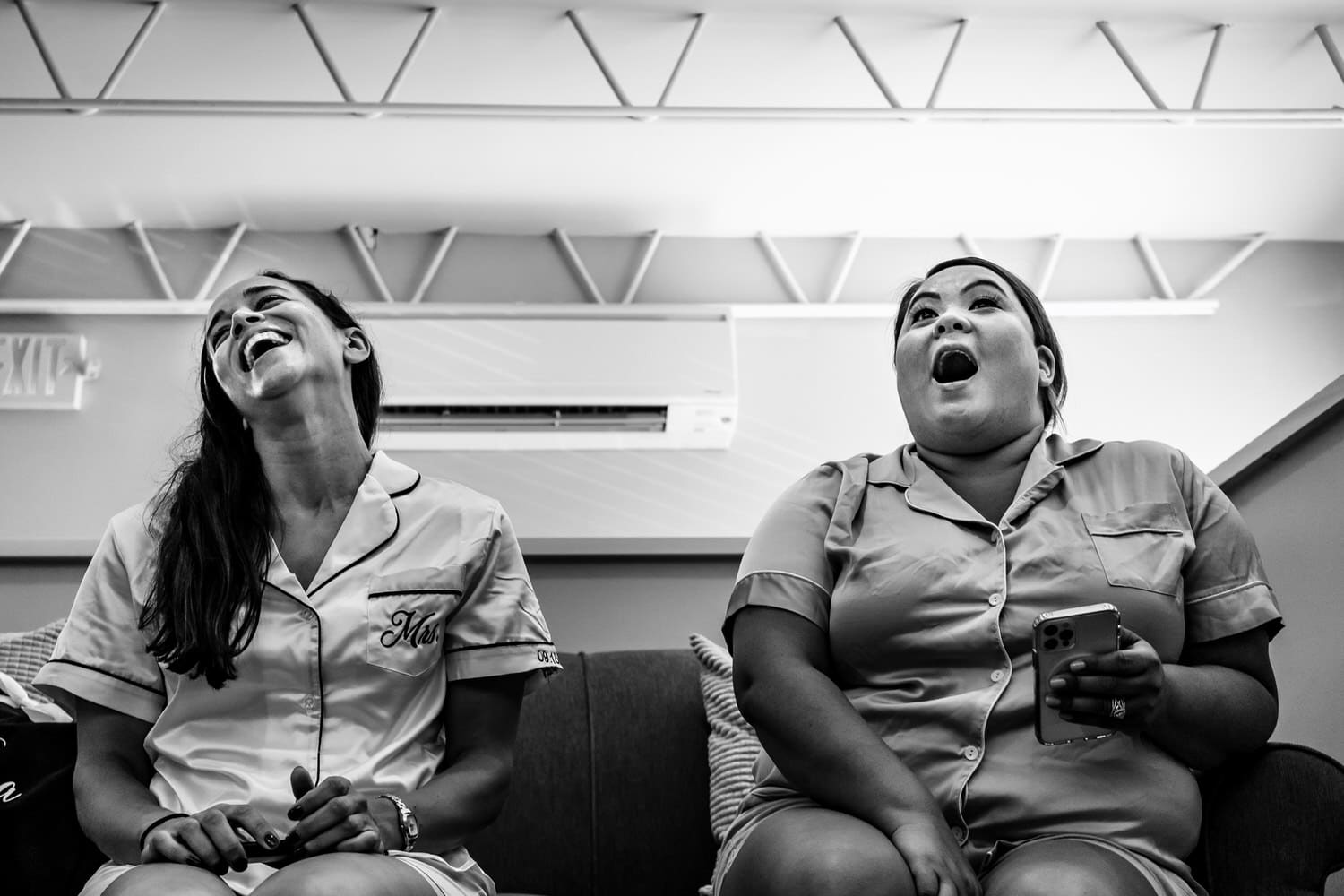 A candid black and white picture of two women sitting on a couch laughing. 