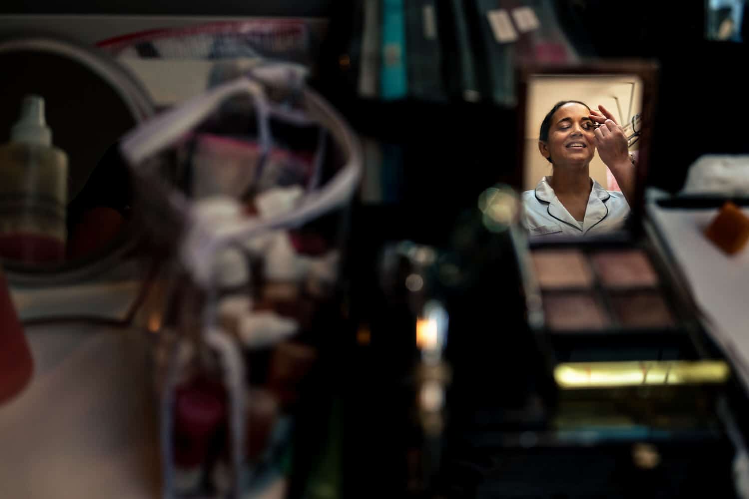 A reflection of a woman in a makeup compact getting eye shadow applied on the morning of her wedding day. 