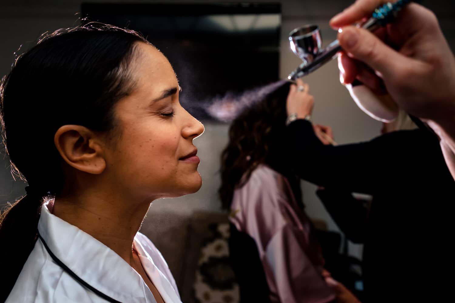 A candid, colorful picture of a woman getting airbrush foundation applied on the morning of her wedding. 