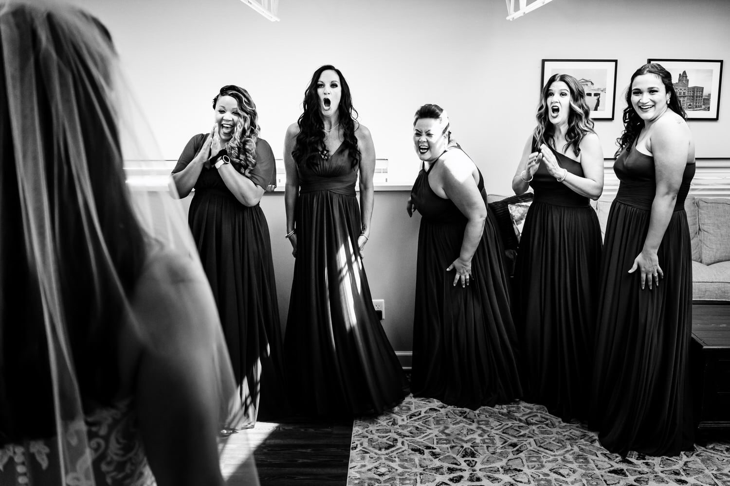 A candid black and white picture of a group of bridesmaids excitedly reacting to seeing the bride for the first time on a summer wedding day at 28 Event Space in Kansas City. 