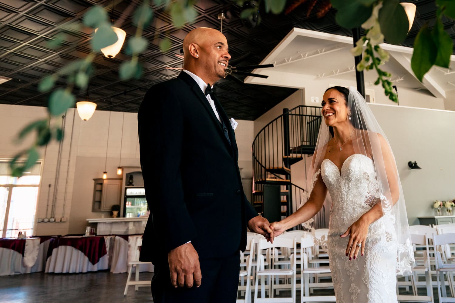 A candid, colorful picture of a bride and groom holding hands and laughing together on their summer wedding day at The Station in Kansas City. 