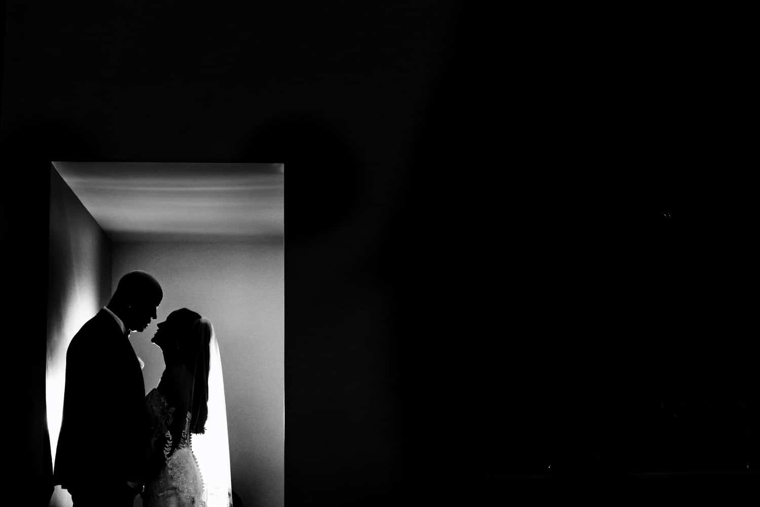 A black and white silhouette of a bride and groom sharing an embrace on their wedding day. 