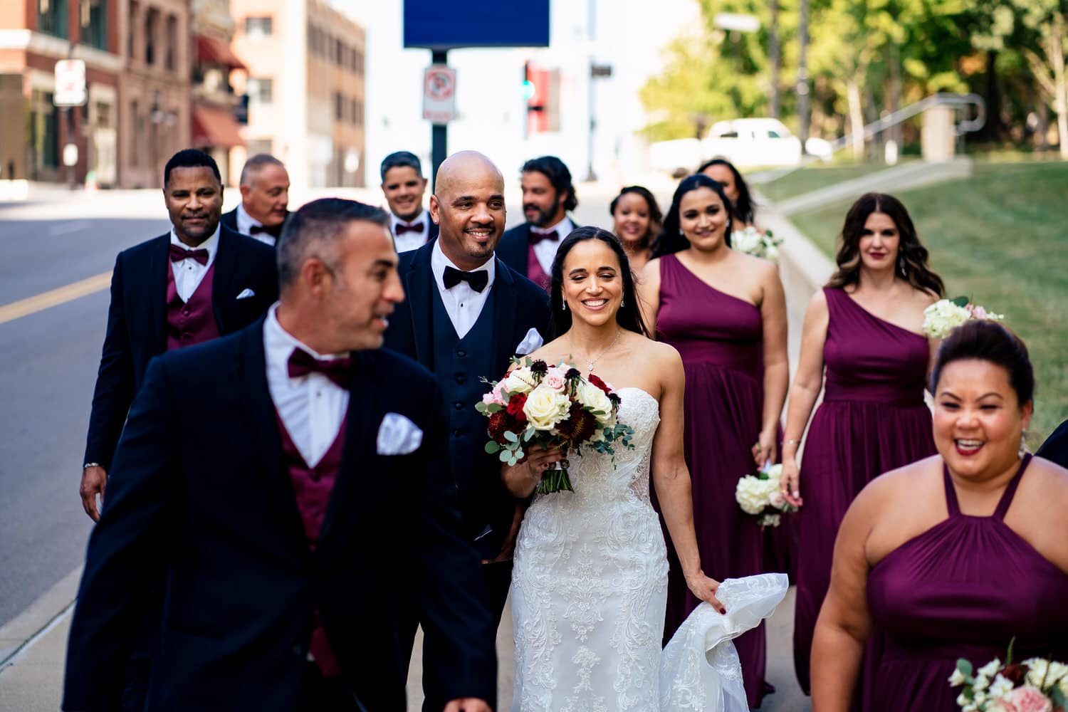 A candid, colorful picture of a bride, groom, and their wedding party walking down a city street in Kansas City on their summer wedding day. 