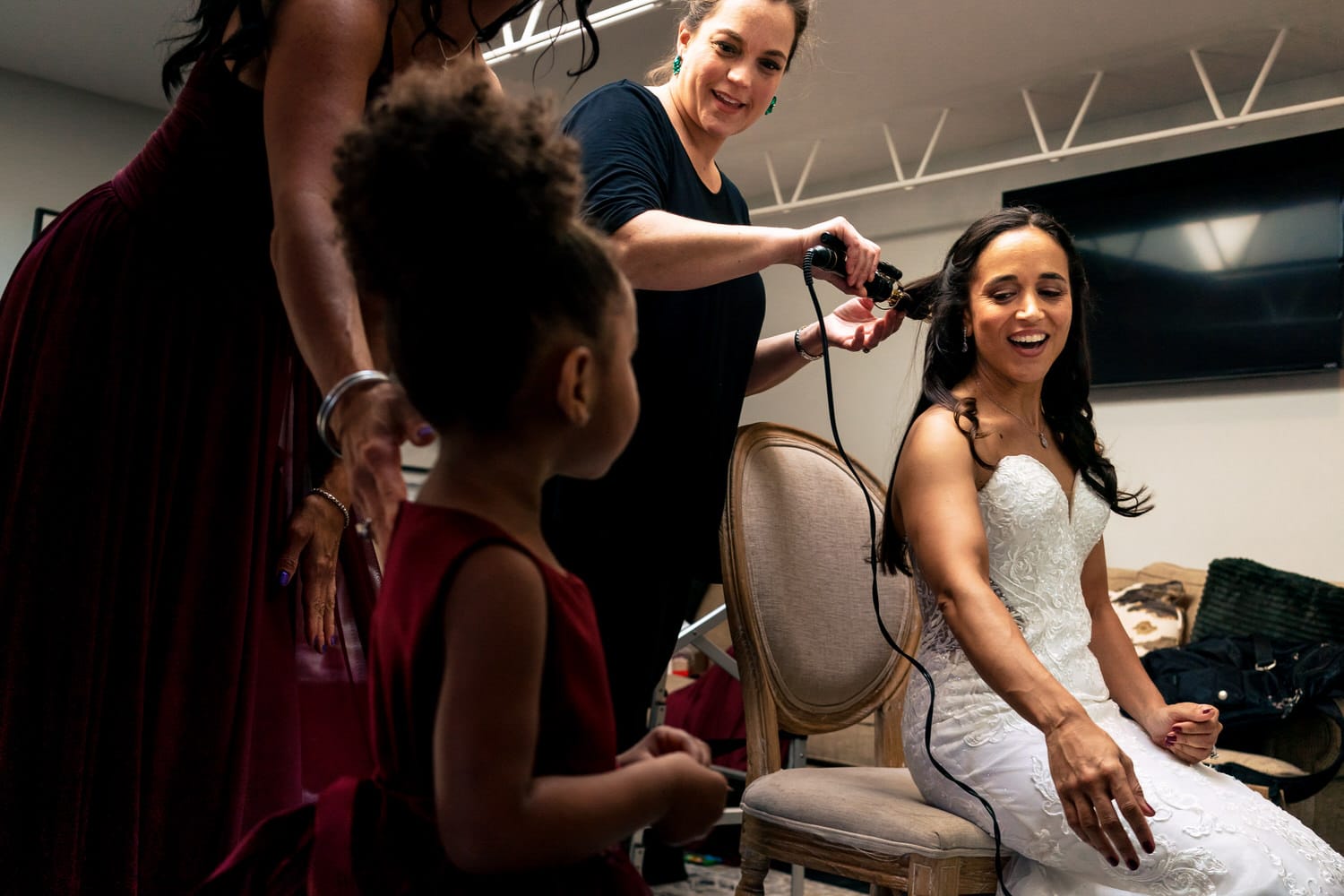 A candid picture of a bride getting her hair curled on her wedding day as she greets her flower girl. 