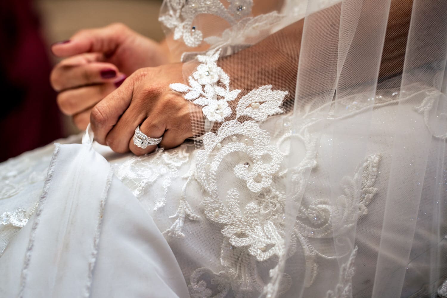 A close up, candid picture of a bride clutching her wedding gown, her red finger nails and engagement ring visible. 