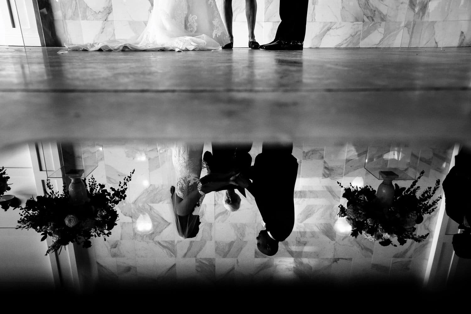 A picture of a reflection of a bride and groom holding hands during a summer wedding ceremony at The Station in Kansas City. 