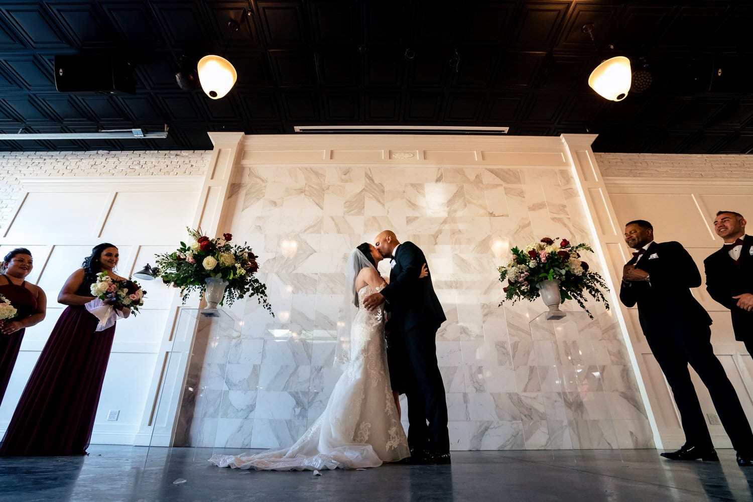 A wide, candid picture of a bride and groom sharing a kiss during their summer wedding ceremony at The Station in Kansas City. 
