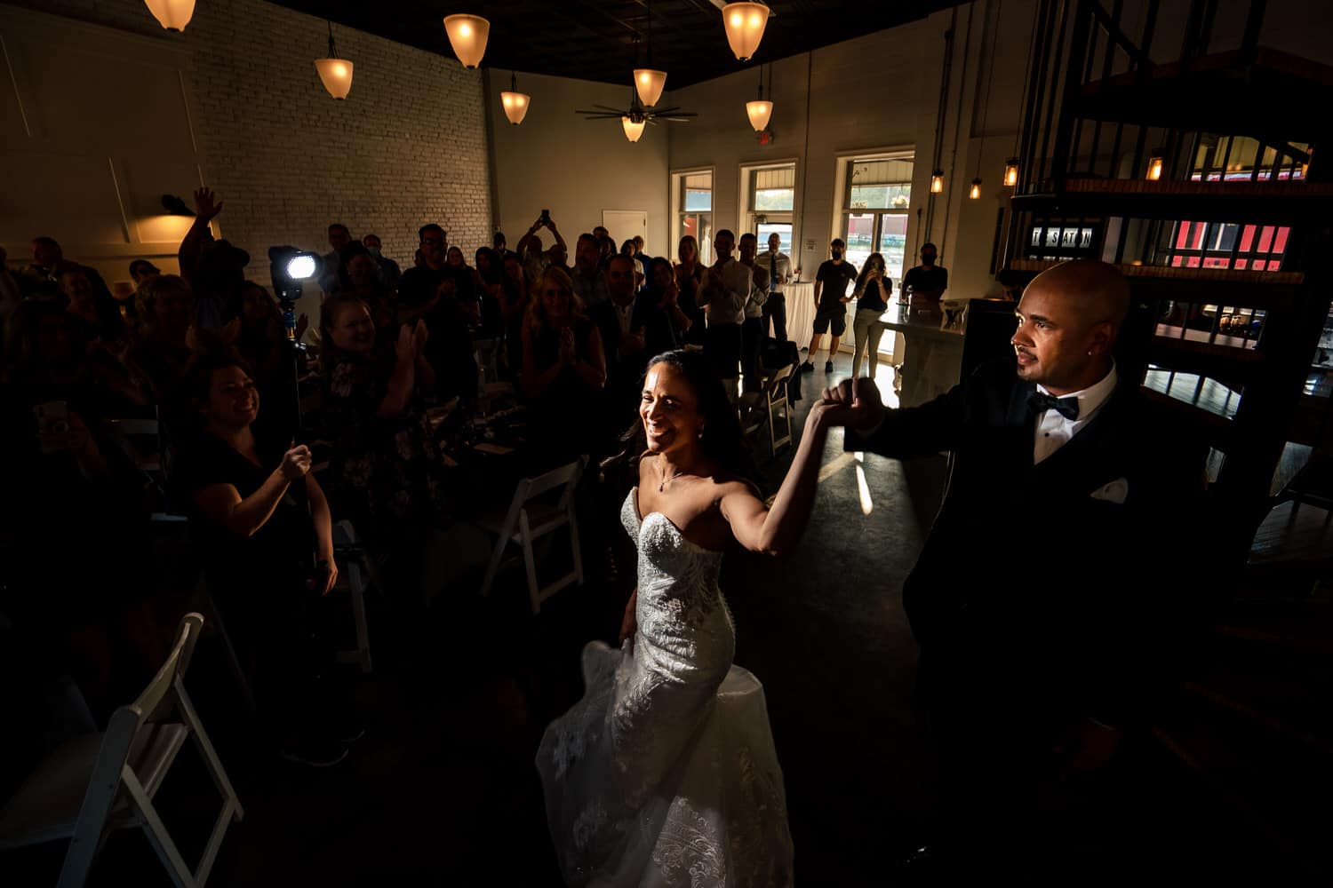 A candid picture of a bride and groom walking into their wedding reception to family and friends cheering. 