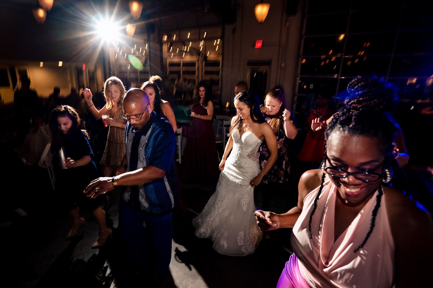 A candid, colorful picture of wedding guests dancing on the dancefloor during a wedding reception at The Station at 28 Event Space in Kansas City. 
