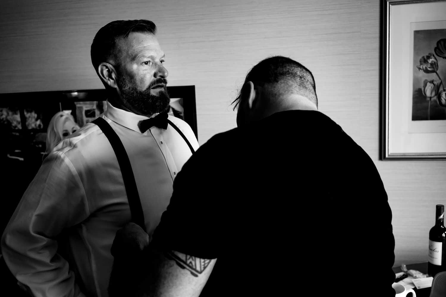 A candid black and white picture of a groom's partner adjusting his suspenders on the morning of their fall wedding in Kansas City. 