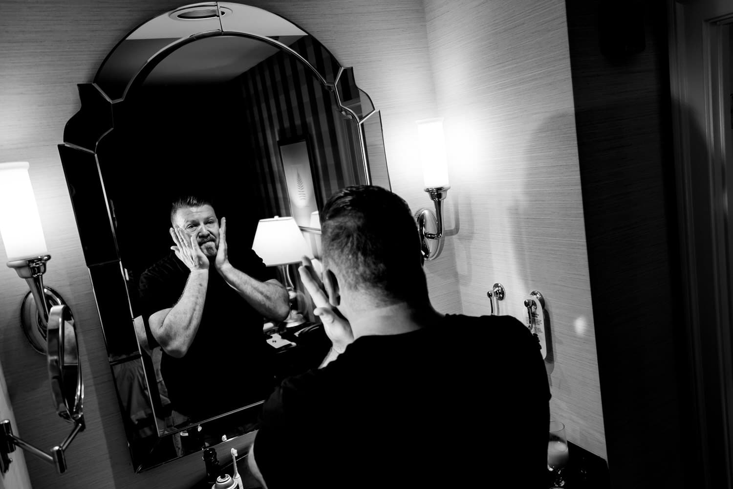 A candid black and white picture of a groom patting his face with aftershave on the morning of his fall wedding at The Madrid. 