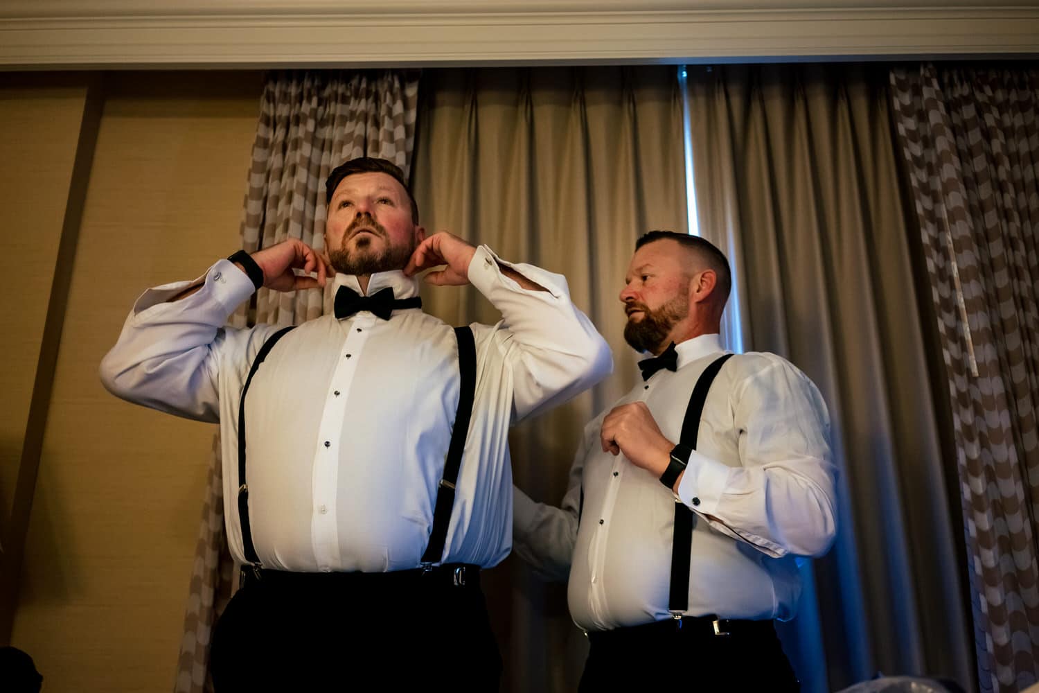 A colorful, candid picture of two grooms adjusting their bowties on the morning of their wedding. 