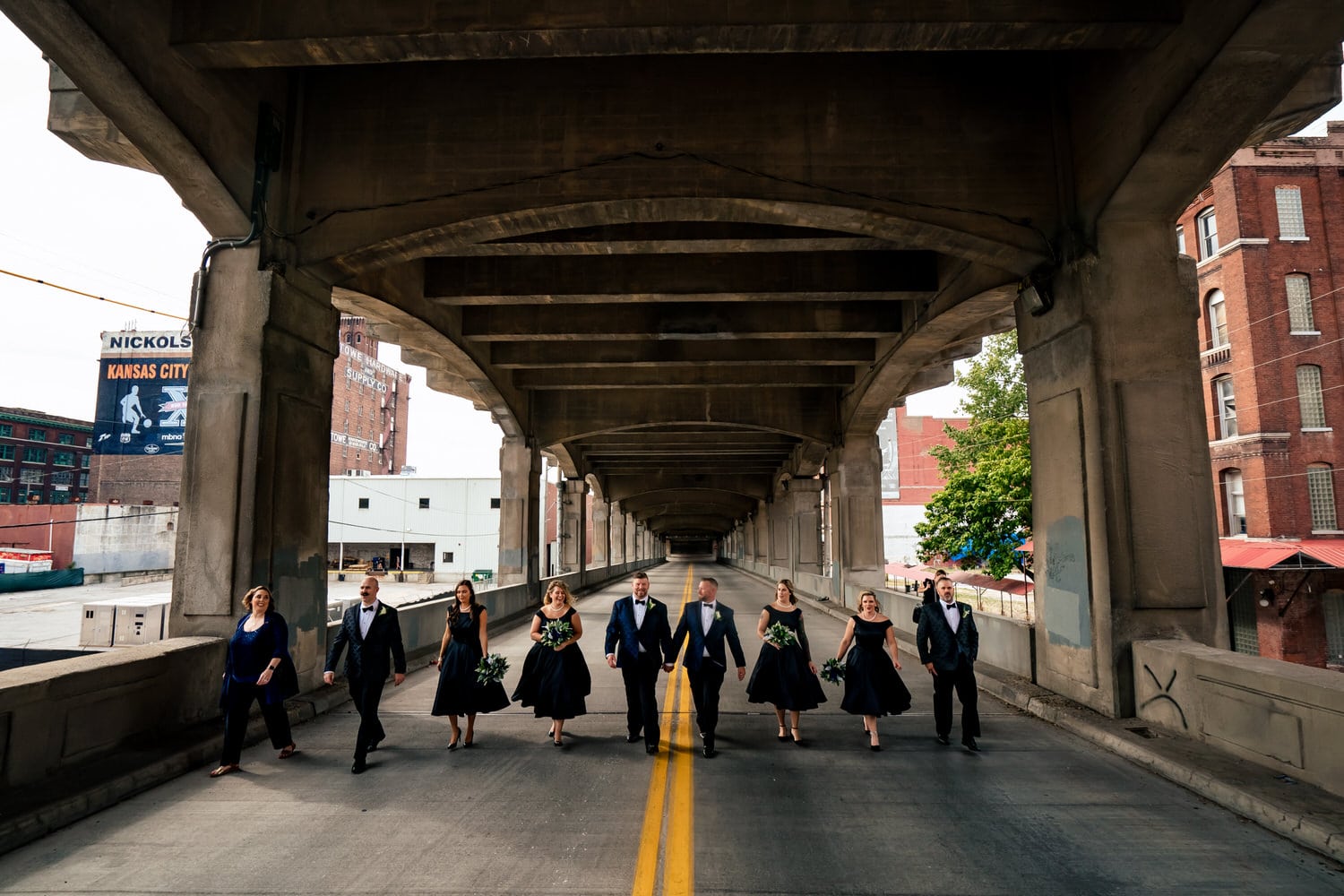 A wide, candid picture of a wedding party walking down the middle of the 12th Street Viaduct on a fall wedding day in October. 
