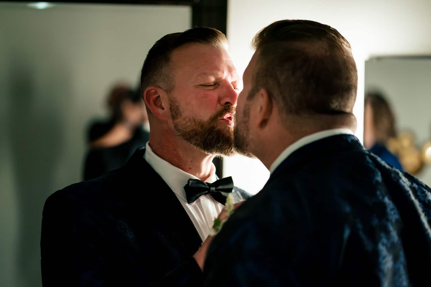 A candid picture of two grooms leaning in to share a quick kiss moments before their wedding ceremony starts at The Madrid Theatre. 