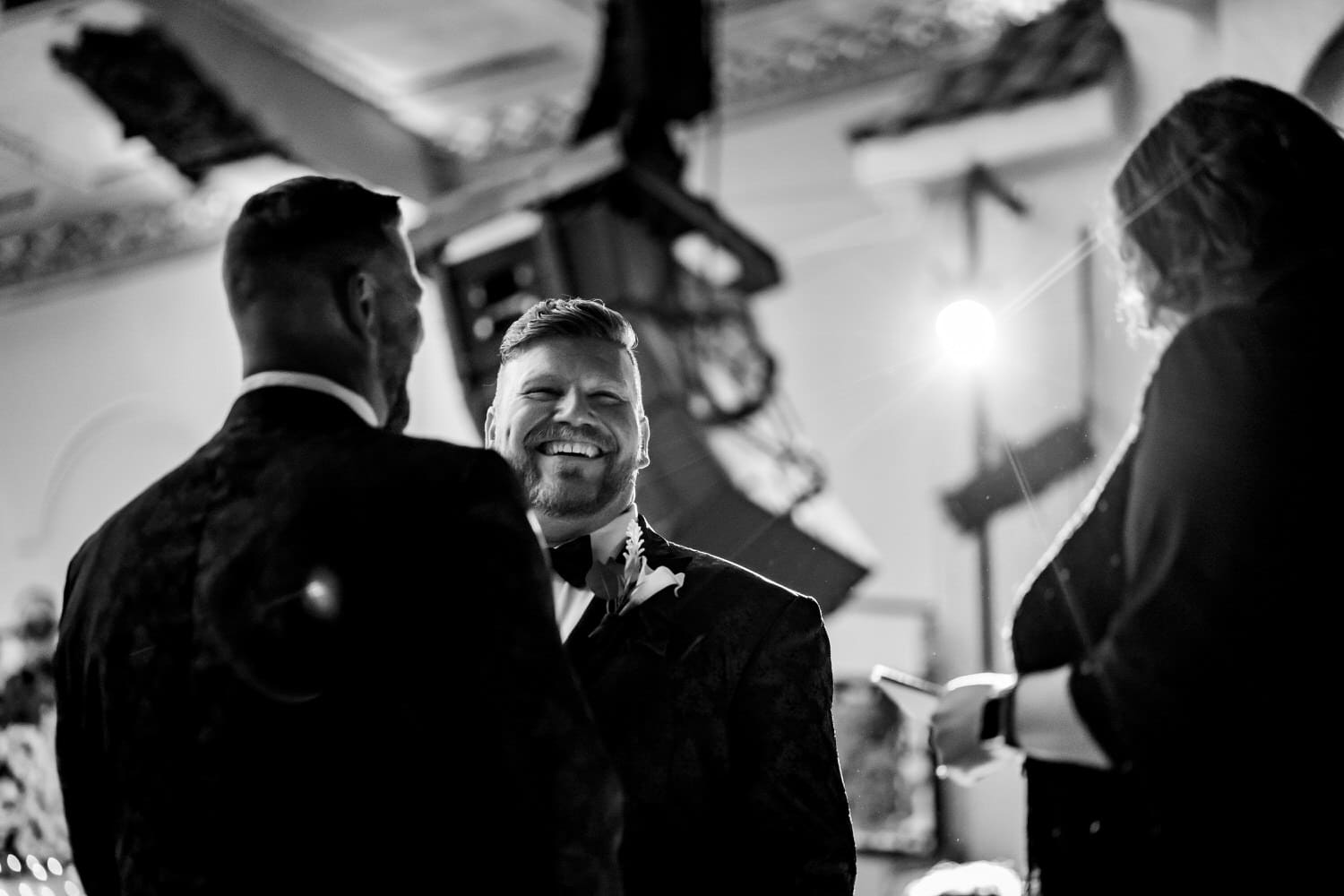 A candid black and white picture of two grooms exchanging vows during their fall wedding at The Madrid Theatre in Kansas City. 