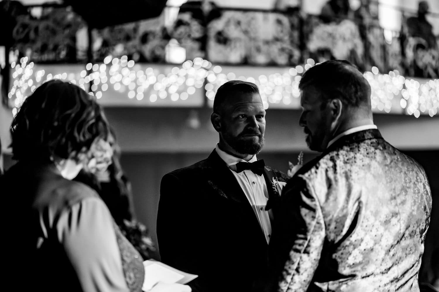 A candid black and white picture of two grooms exchanging vows during their fall wedding at The Madrid Theatre in Kansas City. 