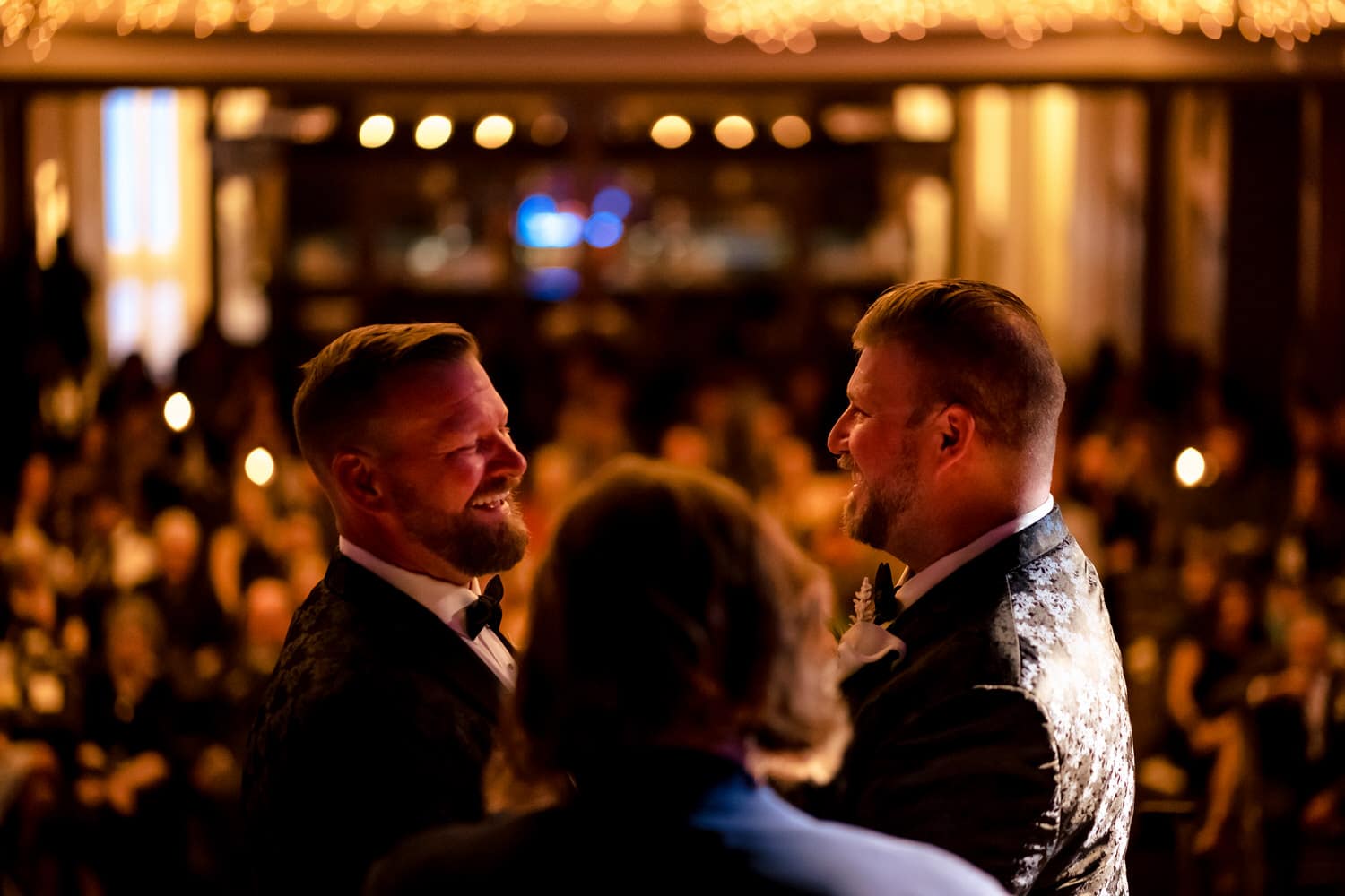 A candid picture of two grooms laughing together at the end of their wedding ceremony at The Madrid Theatre in Kansas City. 