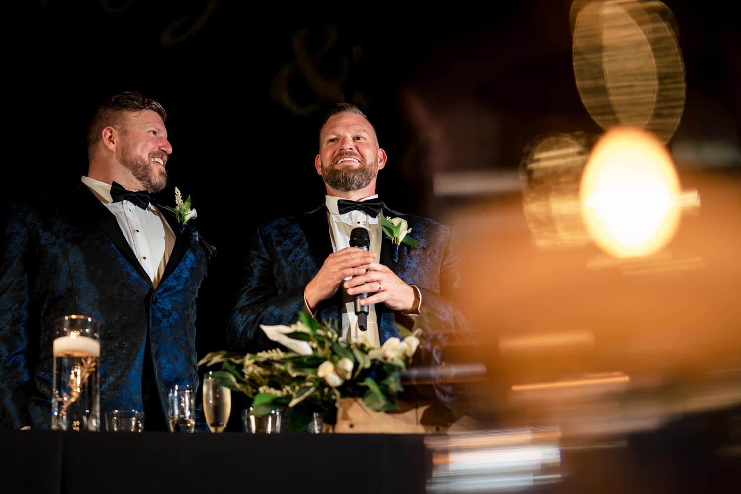 A candid picture of two grooms giving a welcome speech at their reception at The Madrid Theatre in Kansas City on their fall wedding day. 