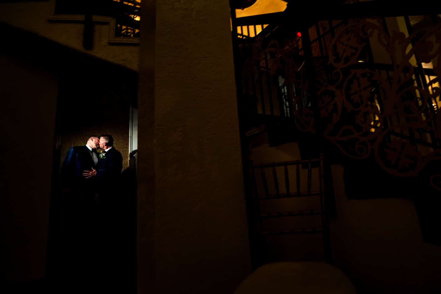 A wide portrait of two grooms leaning in to share a kiss at The Madrid Theatre on their fall wedding day. 