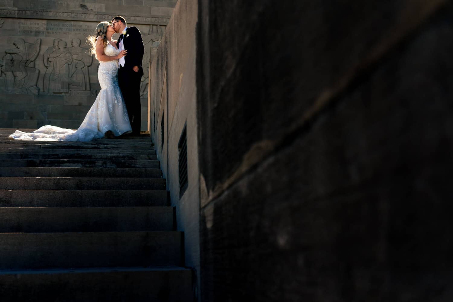 A formal portrait of a bride and groom standing at the top of a set of stone stairs at Liberty Memorial in Kansas City on their fall wedding day. 